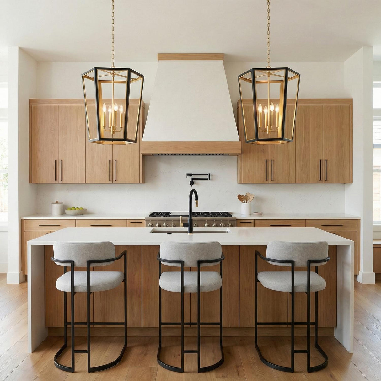 A transitional kitchen features two Rawlin Medium Lantern Pendants in matte black and brushed brass over the island with a white waterfall countertop and light wood cabinetry.