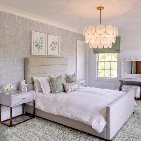 A transitional bedroom featuring the Ophelia Large Chandelier 28", Modern Brass and Layered Glass hanging above a beige upholstered bed with green patterned accent pillows.