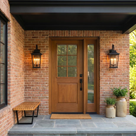 A traditional red brick entry featuring two Pembroke Large Outdoor Wall Light 26", Textured Black lanterns flanking a wood front door at twilight with ceramic planters.