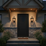 Fairmont Small Outdoor Wall Light 16, Textured Black - Two black lanterns with warm lighting flank a black front door with stone and stucco siding.
