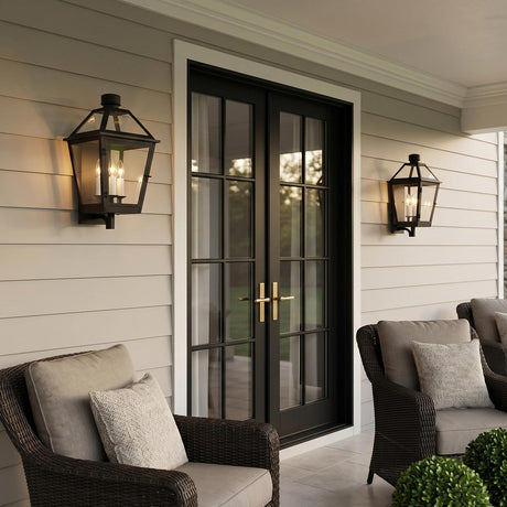 A traditional patio featuring Fairmont Medium Outdoor Wall Light 20 inch fixtures in textured black flanking black French doors on beige siding with wicker armchairs at dusk.