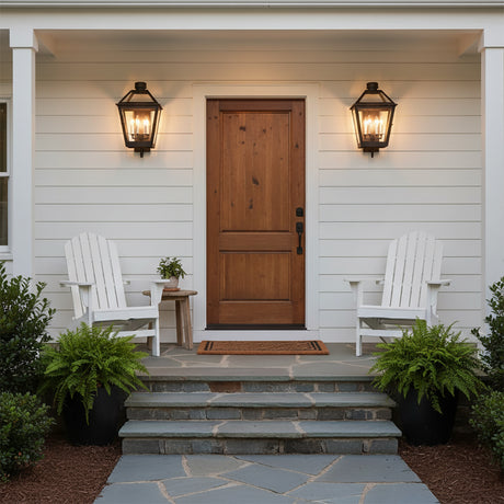 Fairmont Large Outdoor Wall Light 24 - Two black lanterns flanking a natural wood door on a white exterior with Adirondack chairs and potted ferns.