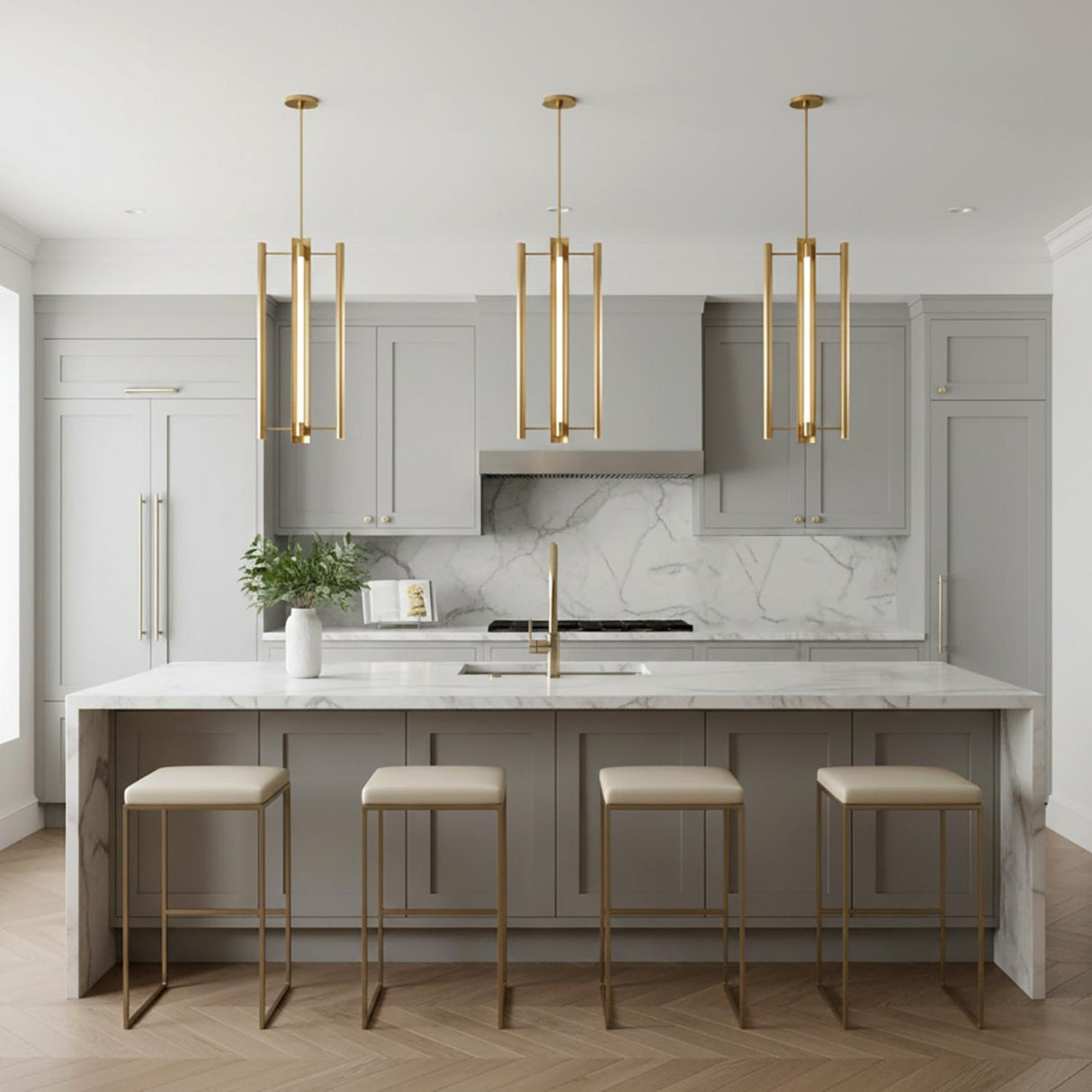 A modern kitchen featuring three Robin Elongated 4 Light LED Pendant 16", Modern Brass fixtures over the island, marble waterfall counters, gray cabinets, and gold stools.