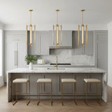 A modern kitchen featuring three Robin Elongated 4 Light LED Pendant 16", Modern Brass fixtures over the island, marble waterfall counters, gray cabinets, and gold stools.