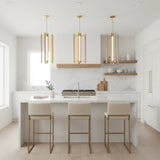 Robin Elongated 4 Light LED Pendant 16" Modern Brass - Three brass pendant lights hang above a kitchen island with bar stools, a marble backsplash, and a wooden range hood.