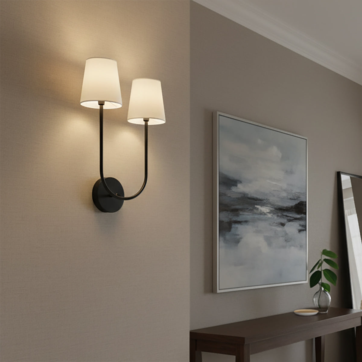 Greta Double Wall Sconce, Black - A modern double wall sconce with black arms and white shades, mounted on a textured taupe wall next to a framed abstract painting.