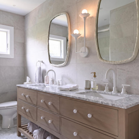 A contemporary bathroom with the Posey Double Wall Sconce 17", Textured White with Rustic Brass Accents installed between two organic mirrors over a light wood double vanity.