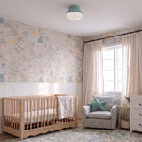 A contemporary bedroom featuring the Skylar Flush Mount 11", Aquaverde with a frosted glass dome on the ceiling above a light wood crib and patterned wallpaper.