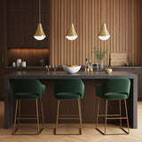 A modern kitchen featuring three Skylar Pendant 11 inch Satin Brass fixtures with frosted glass shades hanging over a dark gray island with green velvet stools.