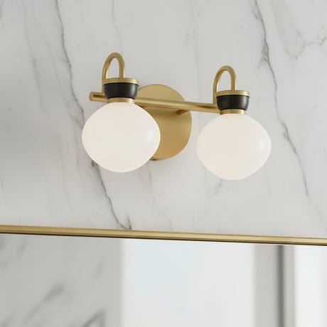 Piper 2 Light Vanity, Satin Brass and Black - A contemporary brass vanity light with two white globe shades is mounted on a marble-patterned wall.