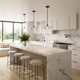 Three glass Alder Pendant lights in Black with Clear Glass shown in a modern kitchen with marble island, stools, and large windows.