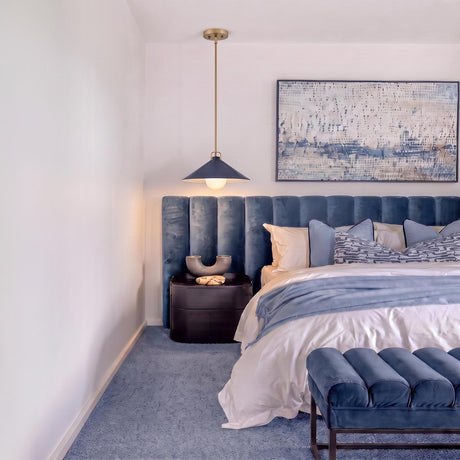 A contemporary bedroom featuring the Nyra Pendant 16", Satin Brass and Navy hanging beside a blue channel-tufted headboard, dark nightstand, and matching velvet bench.