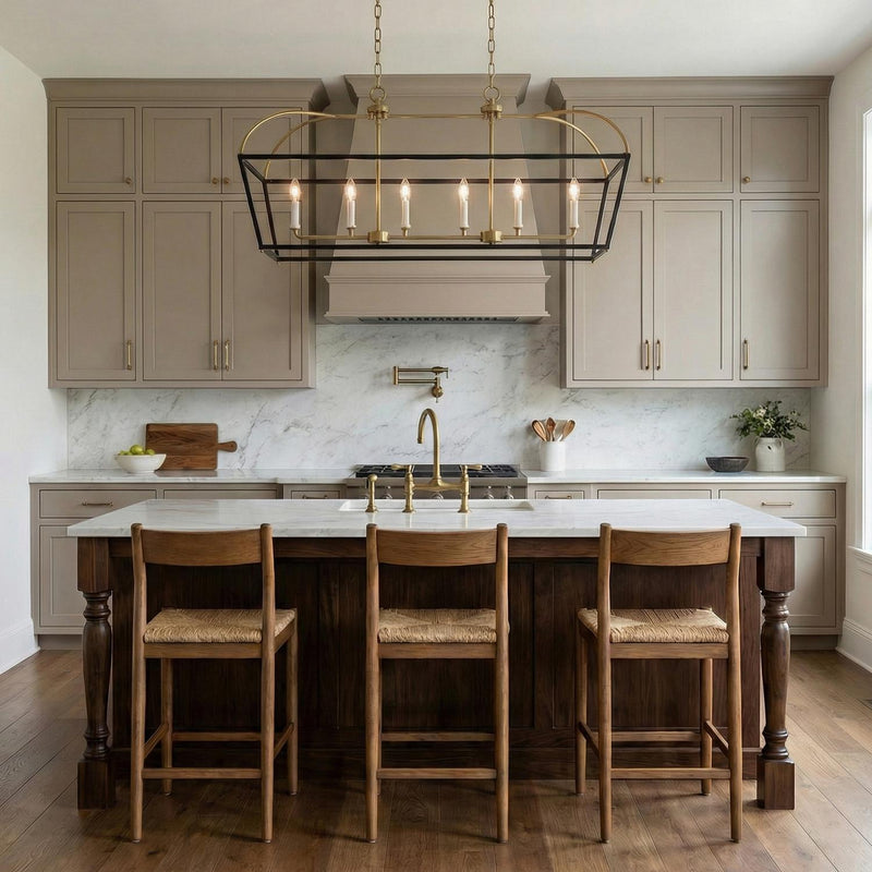 A transitional kitchen features the Langford Linear Lantern Pendant 40" in matte black and satin brass over a white marble island with three wood and wicker stools.