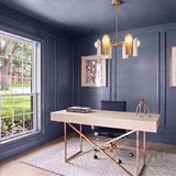 A contemporary office with dark blue paneled walls displays the Kassidy six-light chandelier in satin brass and white above a beige desk and patterned rug.