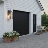 Lorraine Outdoor Wall Light, Large 26" Black - A black lantern-style outdoor wall light illuminates the white siding of a garage with a black door, flanked by potted white flowers.