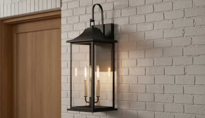 Lorraine Outdoor Wall Light, Large 26" size in Black with clear glass is shown on a light gray brick exterior wall next to a modern wooden front door
