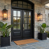 A transitional stone entry with two matte black Lorraine Outdoor Wall Light, Large 26" Black lanterns flanking black double doors at twilight beside large potted greenery.