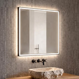 A modern bathroom features the Albin Medium LED Square Mirror with a brushed black frame mounted over a carved stone vessel sink against textured grey tiles.