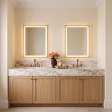 A transitional bathroom featuring two Demott Medium LED Rectangular 22" x 30" brushed brass mirrors over a marble vanity with light wood cabinets and brass faucets.