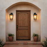 Barrett Outdoor Wall Light, Medium 20" Textured Black - Two black lanterns flanking a rustic wooden door with an arched stucco entryway