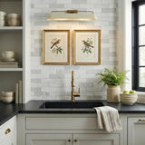 A transitional kitchen features a patina brass and soft sand Henley Picture Light 25" mounted over the sink against a white subway tile backsplash with framed bird prints.