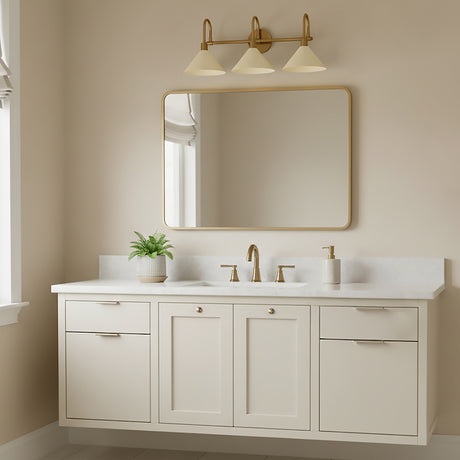 Fletcher 3 Light Vanity, Patina Brass and Soft Sand - A vanity light with three conical shades in a soft sand color hangs above a large rectangular mirror with a brass frame, situated above a cream-colored vanity with brass hardware and a white countertop.
