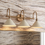 A contemporary bathroom featuring the Fletcher 3 Light Vanity in patina brass and soft sand mounted over a mirror on a veined marble wall.