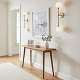 Olivia 2 Light Wall Sconce 24, Aged Brass - Two wall sconces with brass fixtures and white globe lights flanking a framed piece of art above a wooden console table.