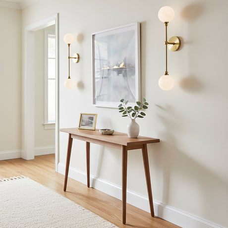Olivia 2 Light Wall Sconce 24, Aged Brass - Two wall sconces with brass fixtures and white globe lights flanking a framed piece of art above a wooden console table.