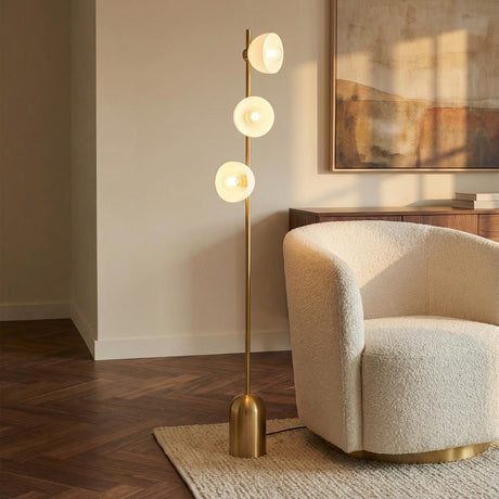 Penrose Floor Lamp, Aged Brass globe floor lamp in a Modern Living Room with a cream bouclé armchair.