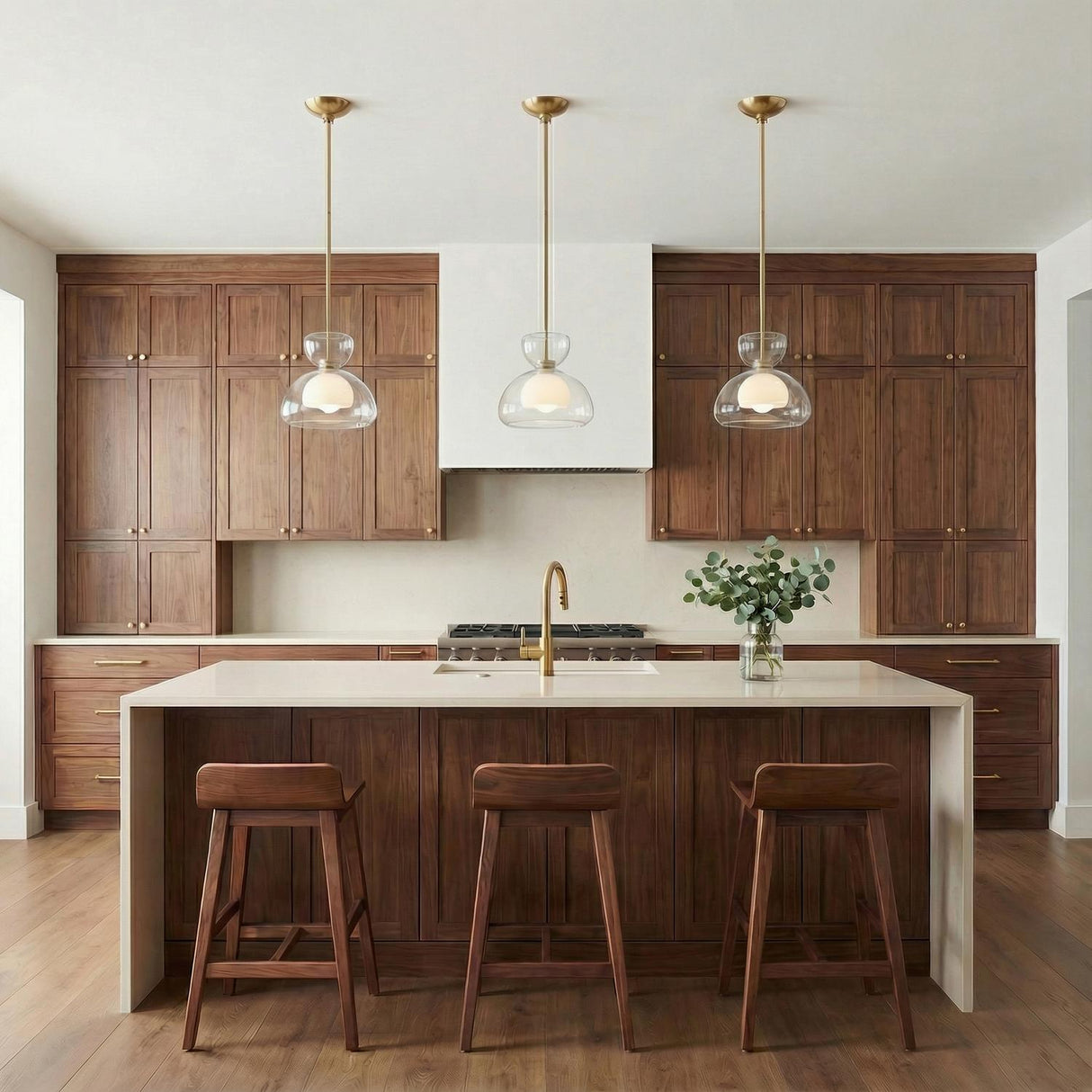 A mid-century kitchen featuring three Rhett Pendant 12", Aged Brass fixtures with clear glass shades over a white waterfall island and walnut cabinetry.
