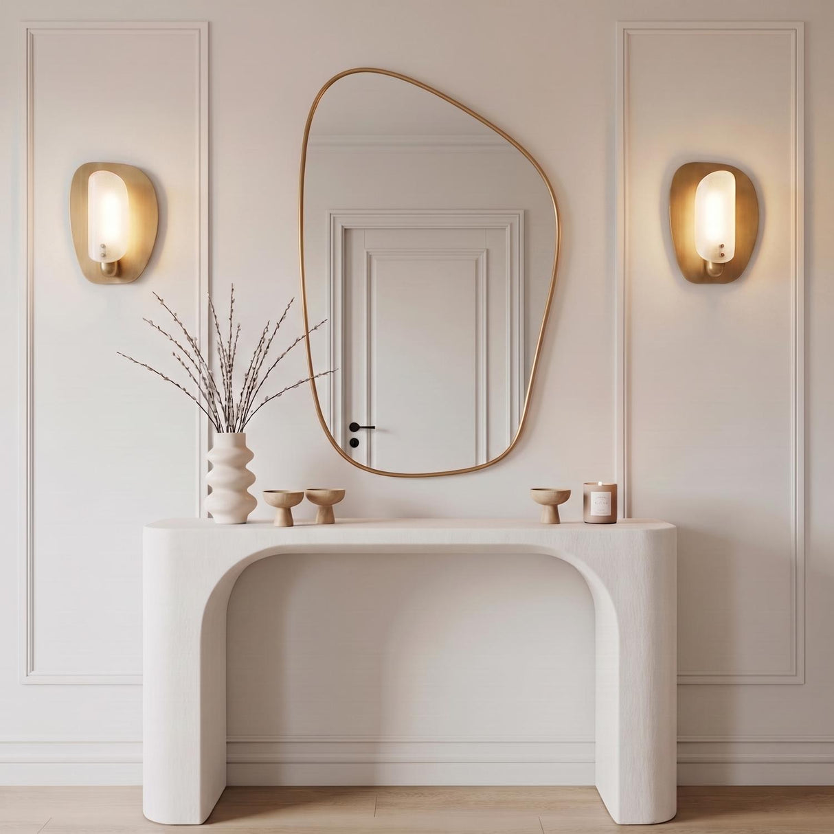 A modern foyer with two Jane Wall Sconces in patina brass flanking an asymmetric gold mirror above a white plaster console table and paneled walls.