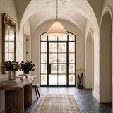 A Mediterranean foyer with the Charlotte Medium Pendant 22", Aged Brass featuring a pleated linen shade hanging from a vaulted ceiling above dark brick flooring.