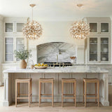 Weathered Gold leaf design pendant in a Transitional Kitchen with a white marble island & natural wood stools.