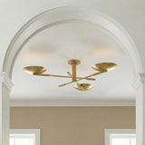 A contemporary entryway featuring the Phoebe aged brass semi-flush mount along the ceiling center framed by a large white archway and beige walls.