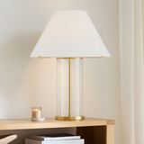 Table lamp is 30" tall with white shade and clear glass with aged brass base, on a wooden console table with books and a candle.