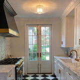 A transitional kitchen with an aged brass and piastra glass flush mount installed along the ceiling center between marble counters and black and white checkered tile.