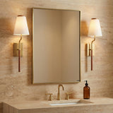 Brushed Brass and brown woven wall sconce in a Transitional Bathroom with a travertine vanity and gold mirror.