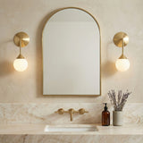 Isabella Wall Sconce 11", Aged Brass with Art Glass globe Wall Sconce in a Transitional Bathroom with an arched mirror and marble vanity.
