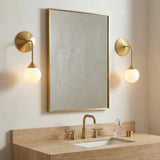 Brushed Brass globe wall sconce in a Contemporary Bathroom with a beige travertine vanity.