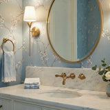 Aria Antique Gold leaf design Wall Sconce in a Transitional Bathroom with a marble vanity and floral wallpaper.