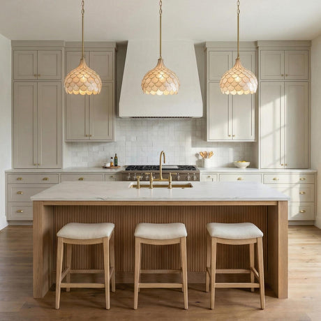 A transitional kitchen with three Valentina Medium Pendant 14", Soft Brass and Capiz Shell fixtures over a fluted wood island with white marble and taupe cabinets.