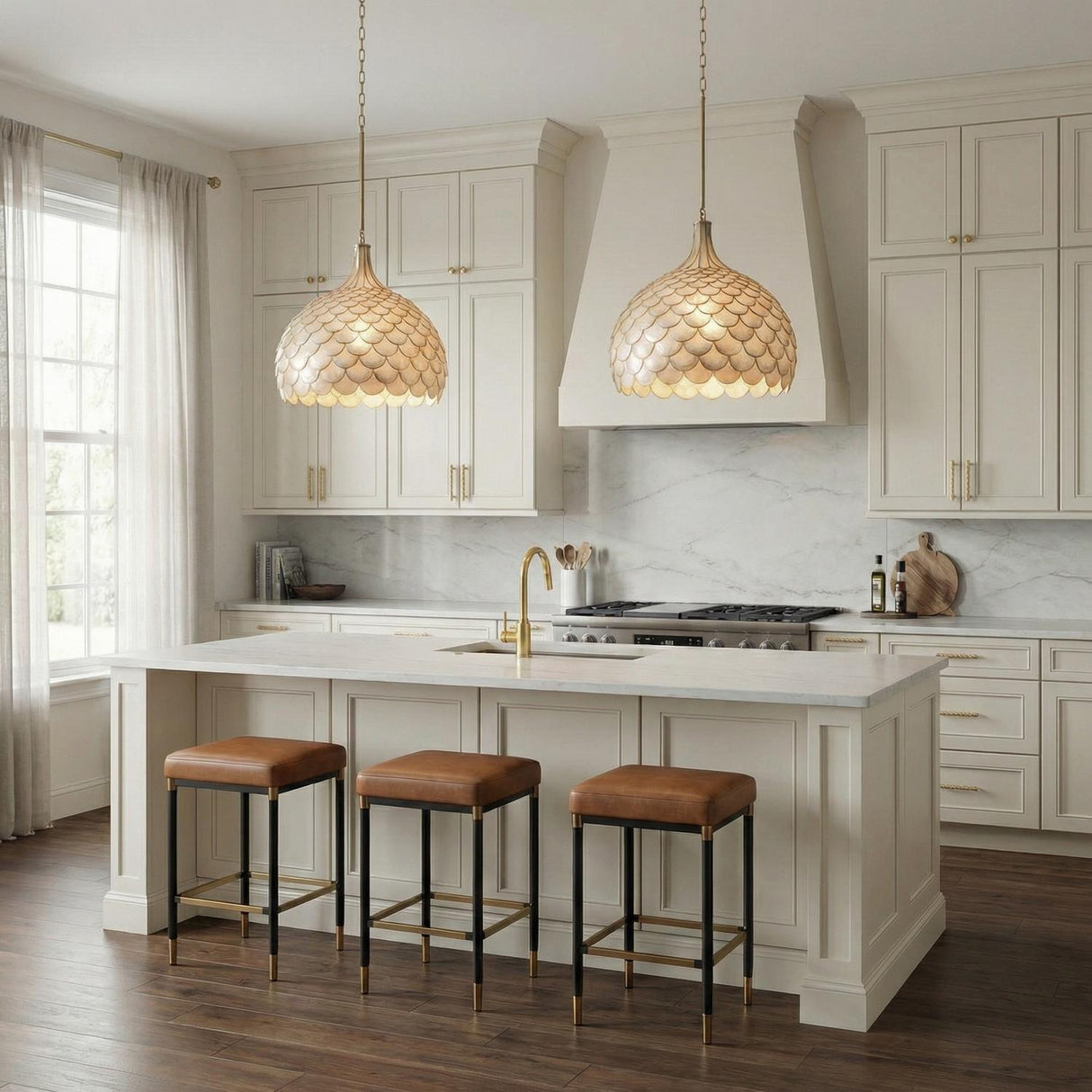 A transitional kitchen features two Valentina Large Pendant 21", Soft Brass and Capiz Shell fixtures over a white marble island with leather stools and cream cabinetry.