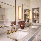 A transitional bathroom with aged brass and frosted glass Abigail LED Wall Sconces mounted between mirrors over a marble vanity with white subway tile.