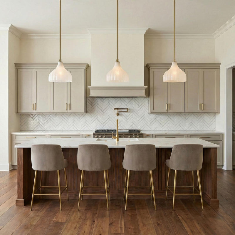 A transitional kitchen features three Claire Medium Pendant 15", Brass and Strie Glass fixtures with brushed brass stems above a marble island and white herringbone tile backsplash.