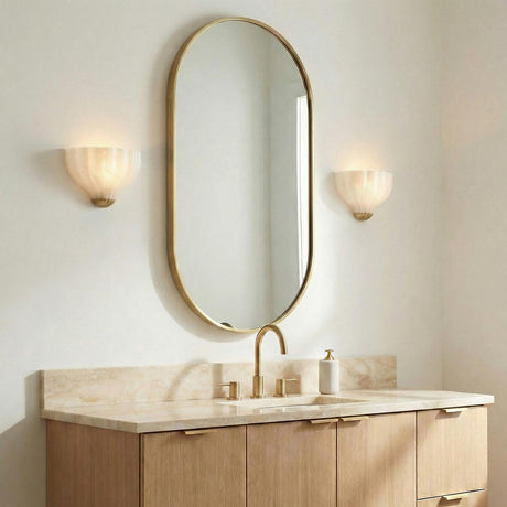Claire Wall Sconce 9", Brass and Strie Glass scalloped Wall Sconce in a Contemporary Bathroom with an oval gold mirror and marble vanity.