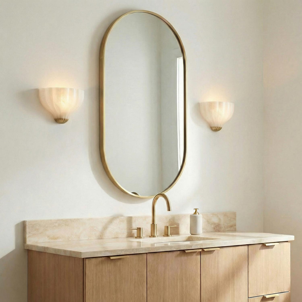 Claire Wall Sconce 9", Brass and Strie Glass scalloped Wall Sconce in a Contemporary Bathroom with an oval gold mirror and marble vanity.