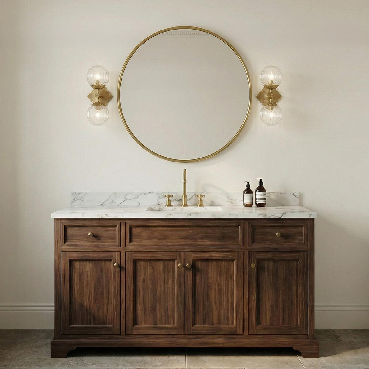 Victoria 2 Light Aged Brass and Clear Ribbed Glass globe Wall Sconce in a Traditional Bathroom with a white marble vanity and gold mirror.