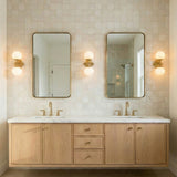 Aurelia Aged Brass ribbed globe wall sconce in a Transitional Bathroom with a light wood double vanity and gold mirrors.