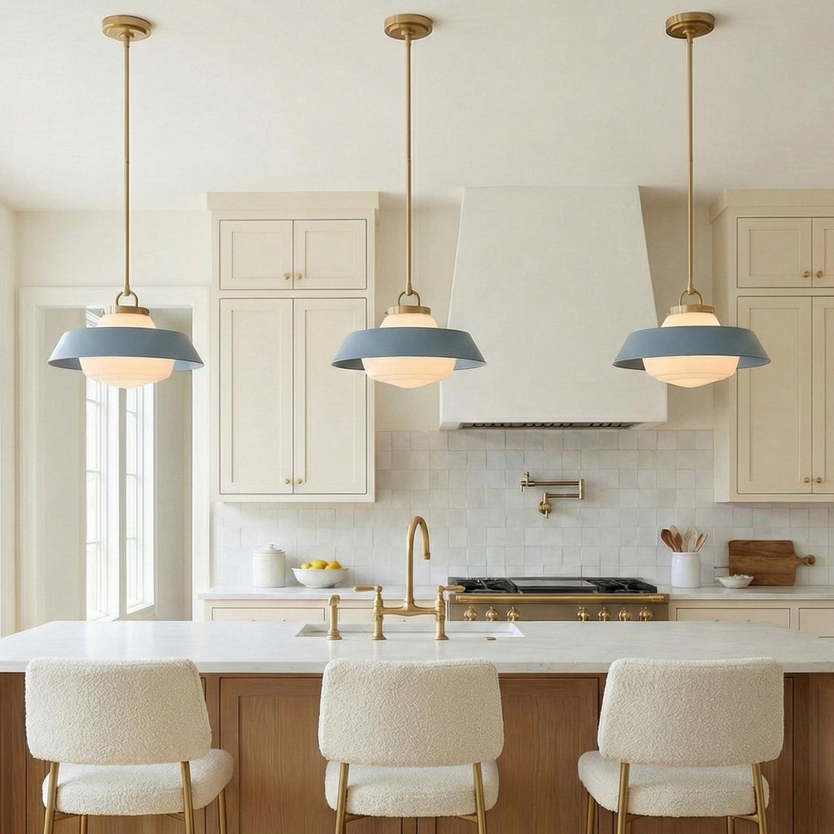 A transitional kitchen features three Blaine Medium Pendant 16", Brass and French Blue fixtures with frosted glass globes over the island, white cabinets, and square tiled backsplash.